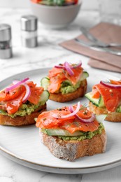 Photo of Delicious sandwiches with salmon, avocado, cucumber and onion on white marble table, closeup