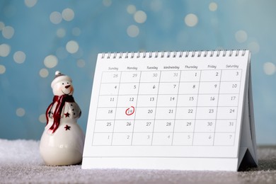Photo of Saint Nicholas Day. Calendar with marked date December 19 and snowman figure on table against blurred lights