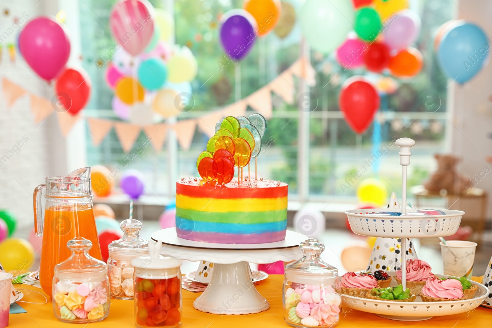 Photo of Bright birthday cake and other treats on table in decorated room