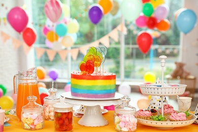 Photo of Bright birthday cake and other treats on table in decorated room