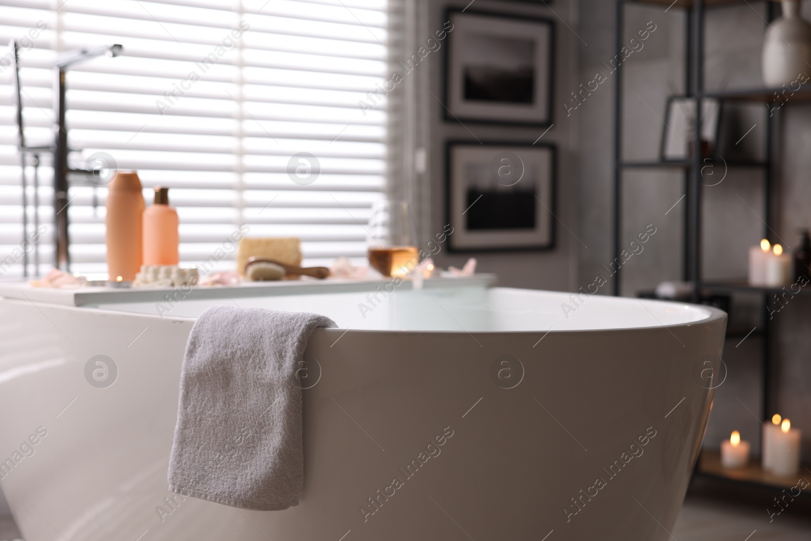 Photo of Wooden tray with wine, toiletries and flower petals on bathtub in bathroom, selective focus