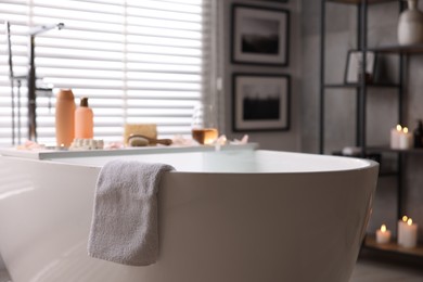 Wooden tray with wine, toiletries and flower petals on bathtub in bathroom, selective focus