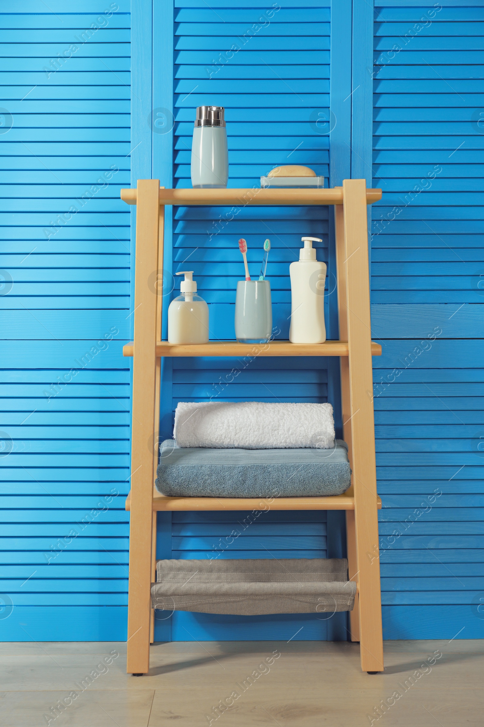 Photo of Wooden shelving unit with toiletries near blue folding screen. Bathroom interior element