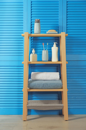 Photo of Wooden shelving unit with toiletries near blue folding screen. Bathroom interior element