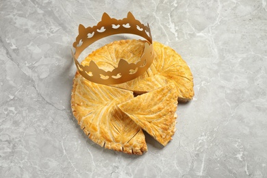 Photo of Traditional galette des Rois with paper crown on light grey marble table, above view