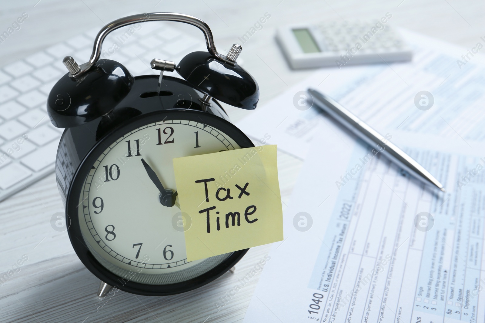 Photo of Alarm clock and reminder note with words Tax Time on white wooden table. Space for text