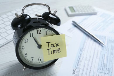 Photo of Alarm clock and reminder note with words Tax Time on white wooden table. Space for text