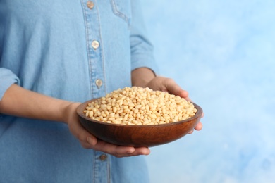 Photo of Woman holding bowl with shelled pine nuts on color background, closeup