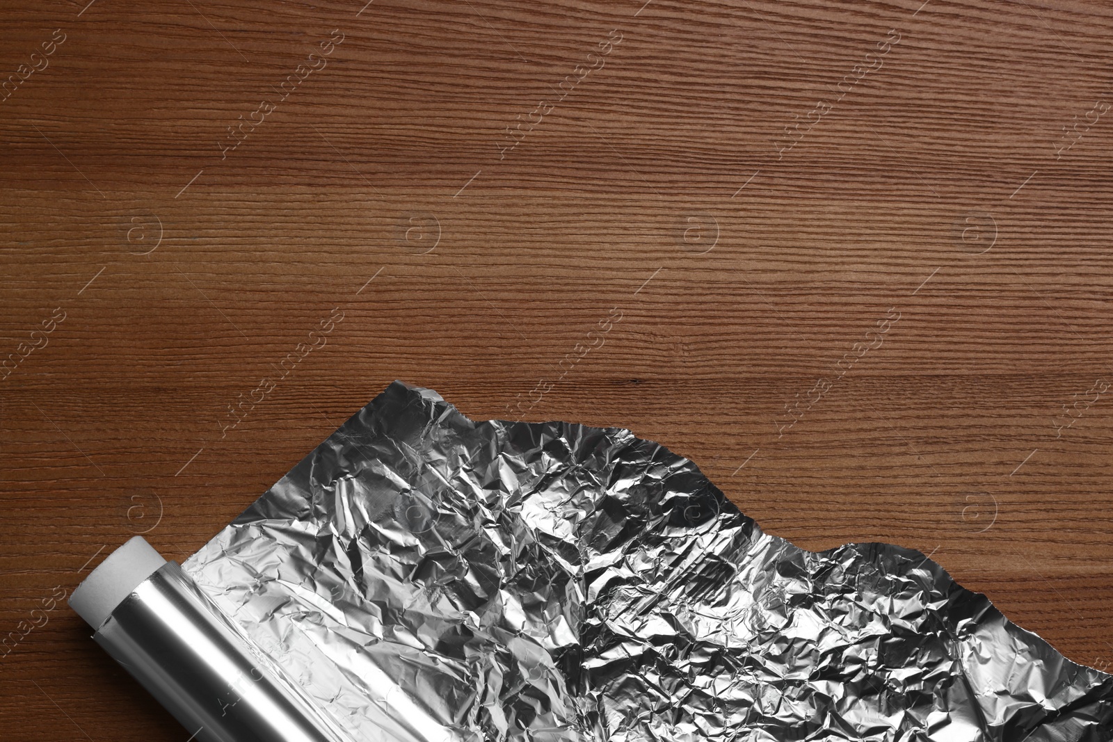 Photo of Roll of aluminum foil on wooden table, top view. Space for text