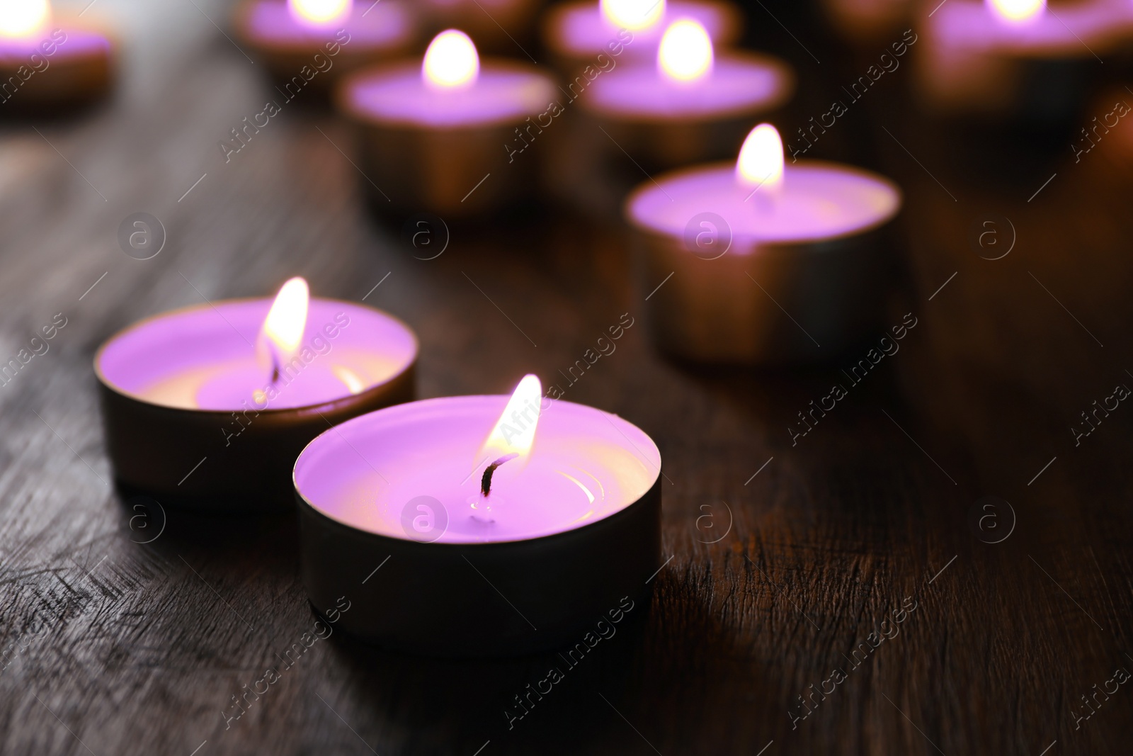 Image of Beautiful burning violet candles on wooden table, closeup. Funeral attributes