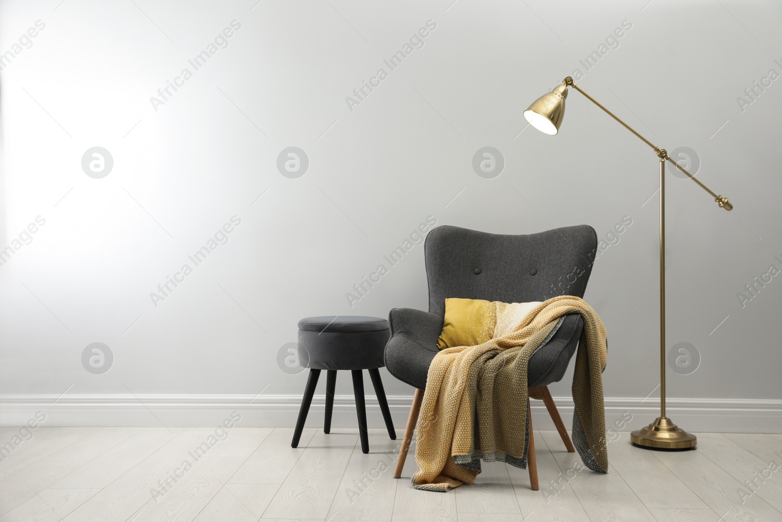 Photo of Stylish armchair with plaid, floor lamp and ottoman near white wall, space for text. Interior design