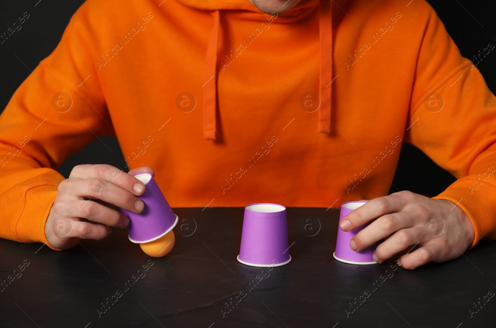 Photo of Shell game. Man showing ball under cup at black table, closeup