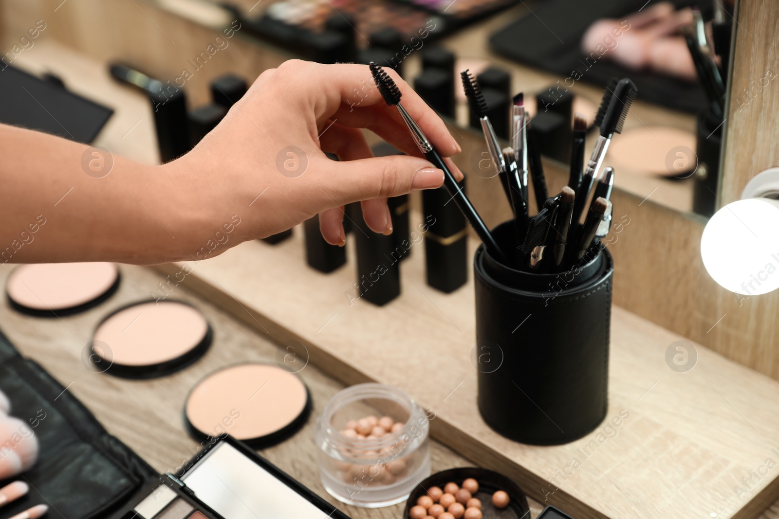 Photo of Professional makeup artist taking brush from holder at wooden table indoors, closeup