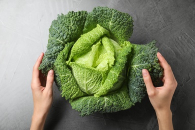 Woman with fresh green savoy cabbage at grey table, top view