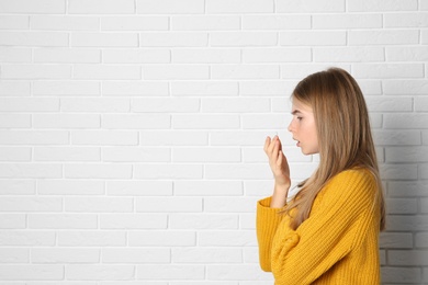Photo of Teenage girl suffering from cough near brick wall. Space for text