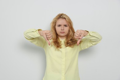 Photo of Dissatisfied young woman showing thumbs down on white background