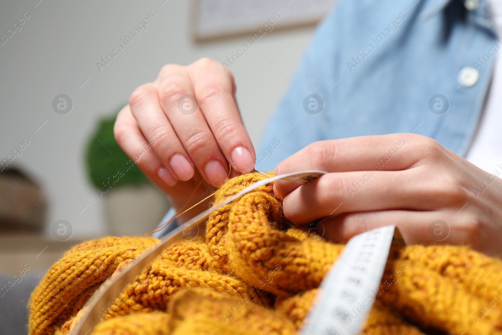 Photo of Woman sewing sweater with needle at home, closeup