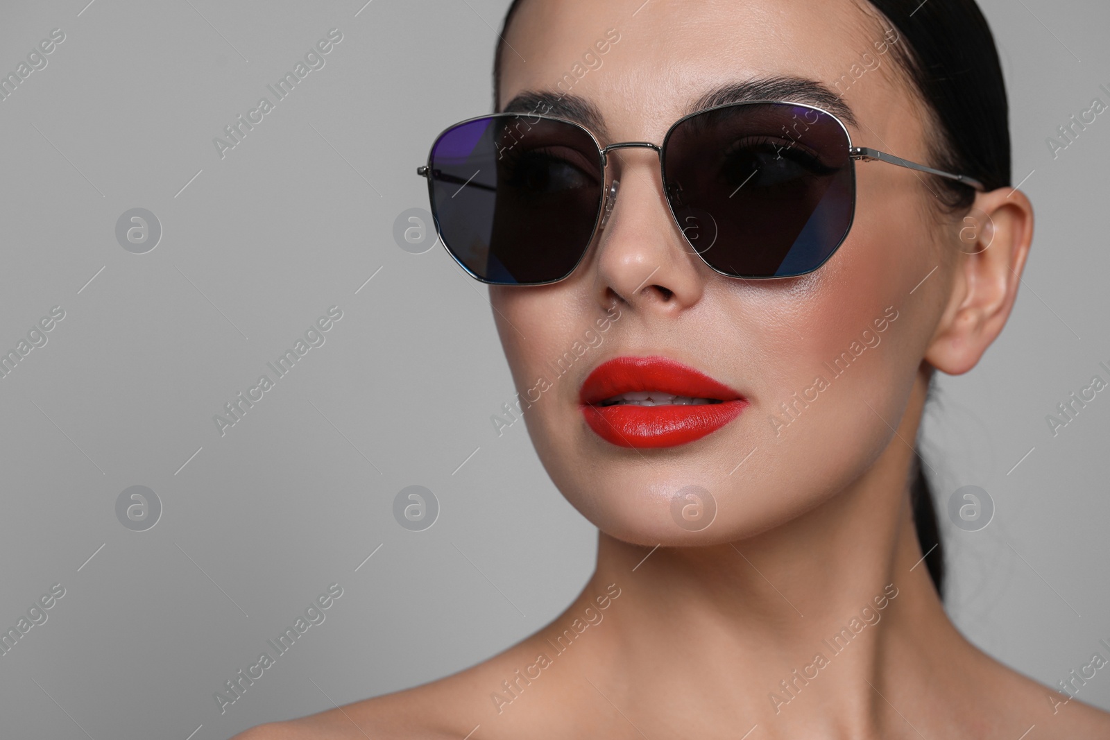 Photo of Attractive woman in fashionable sunglasses against grey background, closeup. Space for text