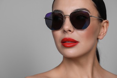 Photo of Attractive woman in fashionable sunglasses against grey background, closeup. Space for text