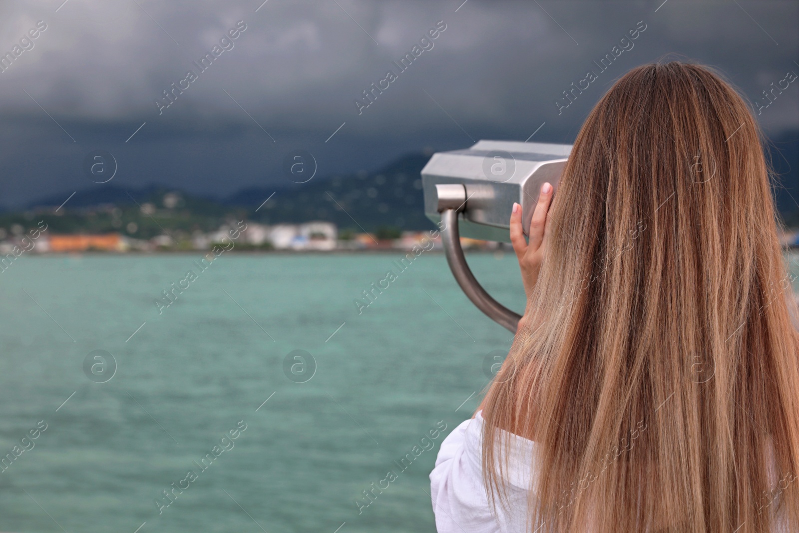 Photo of Woman looking through mounted binoculars at mountains. Space for text