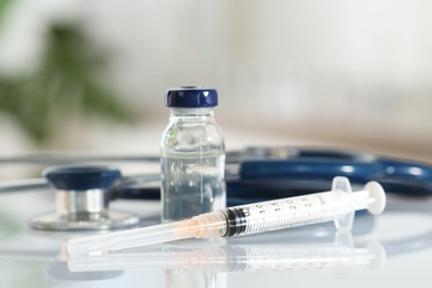 Glass vial, syringe and stethoscope on white table, closeup