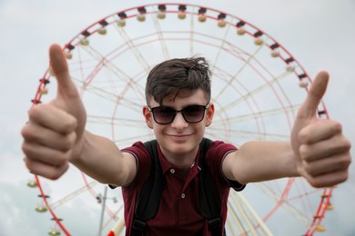 Photo of Teenage boy showing thumbs up against Ferris wheel outdoors
