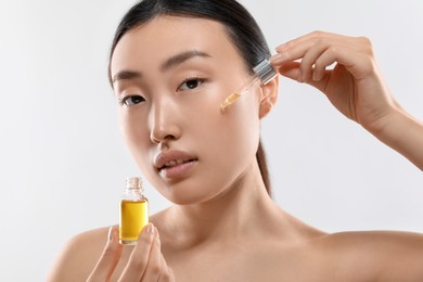 Beautiful young woman applying cosmetic serum onto her face on white background