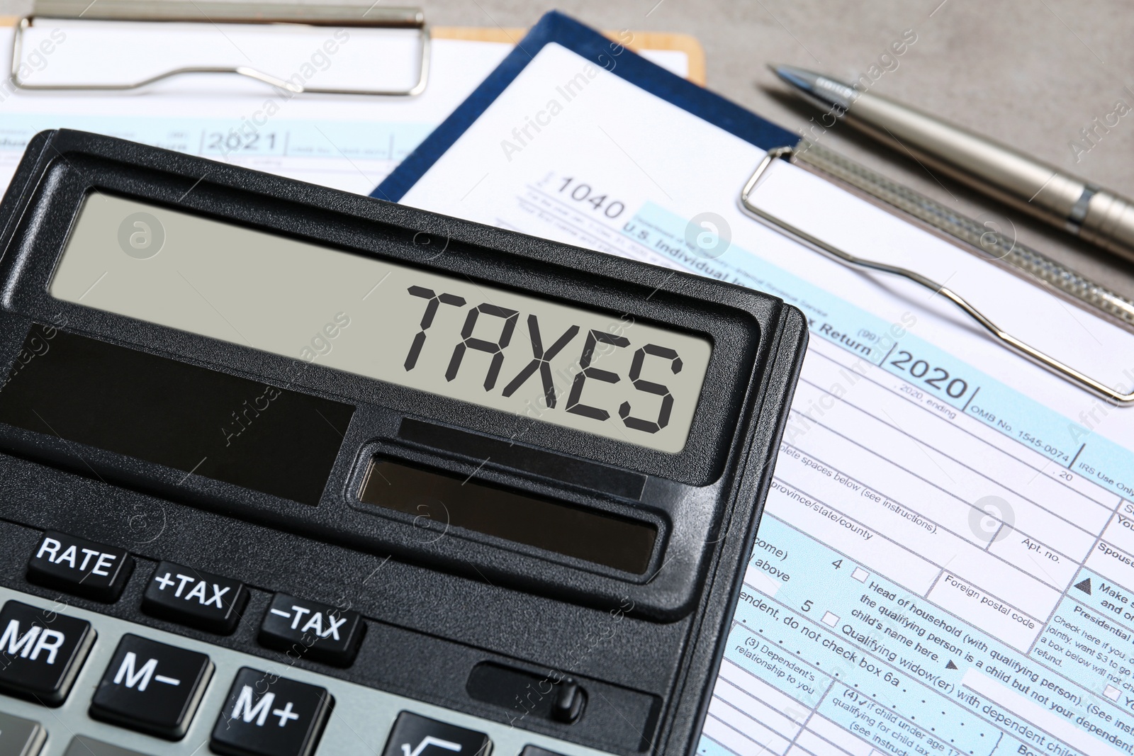 Image of Calculator with word Taxes, documents and pen on table, closeup