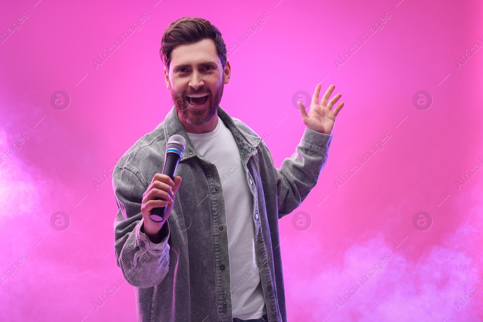 Photo of Handsome man with microphone singing on pink background