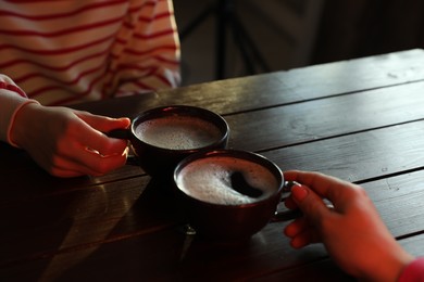 Photo of Women with cups of hot coffee at wooden table, closeup