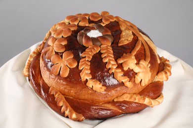 Photo of Korovai on tablecloth against grey background, closeup. Ukrainian bread and salt welcoming tradition