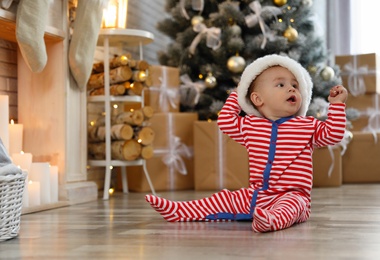 Photo of Little baby wearing Santa hat on floor at home. First Christmas