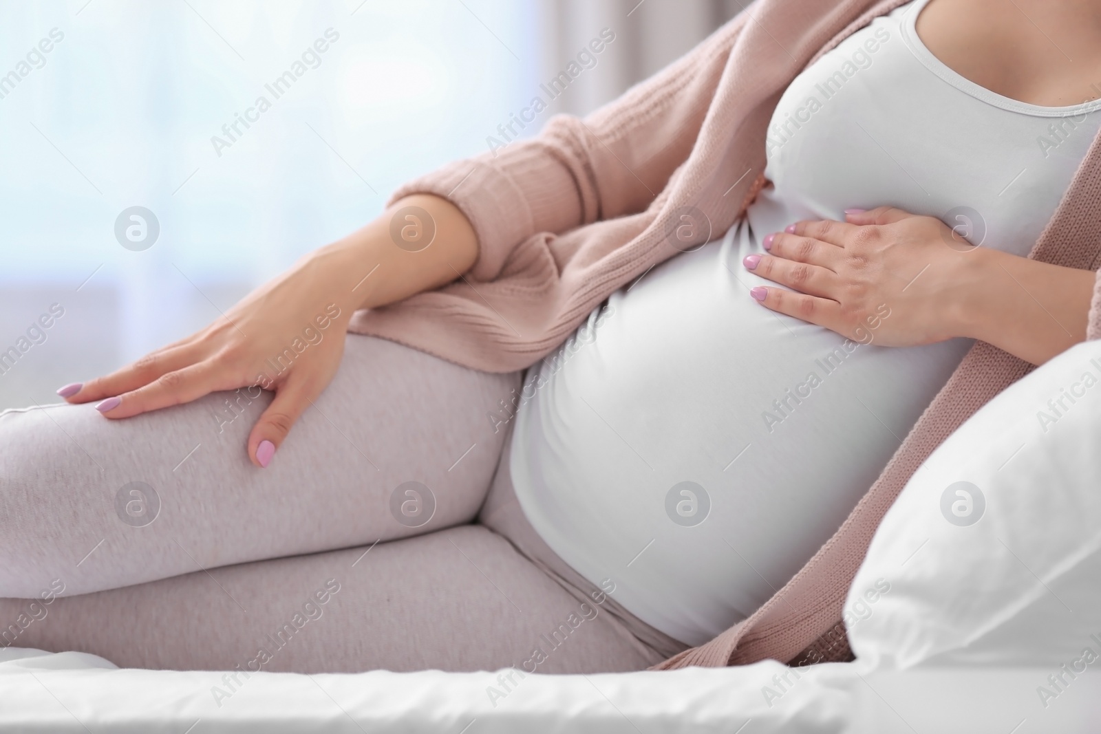 Photo of Young pregnant woman lying on bed and touching her belly at home, closeup