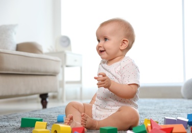 Cute baby girl playing with building blocks in room
