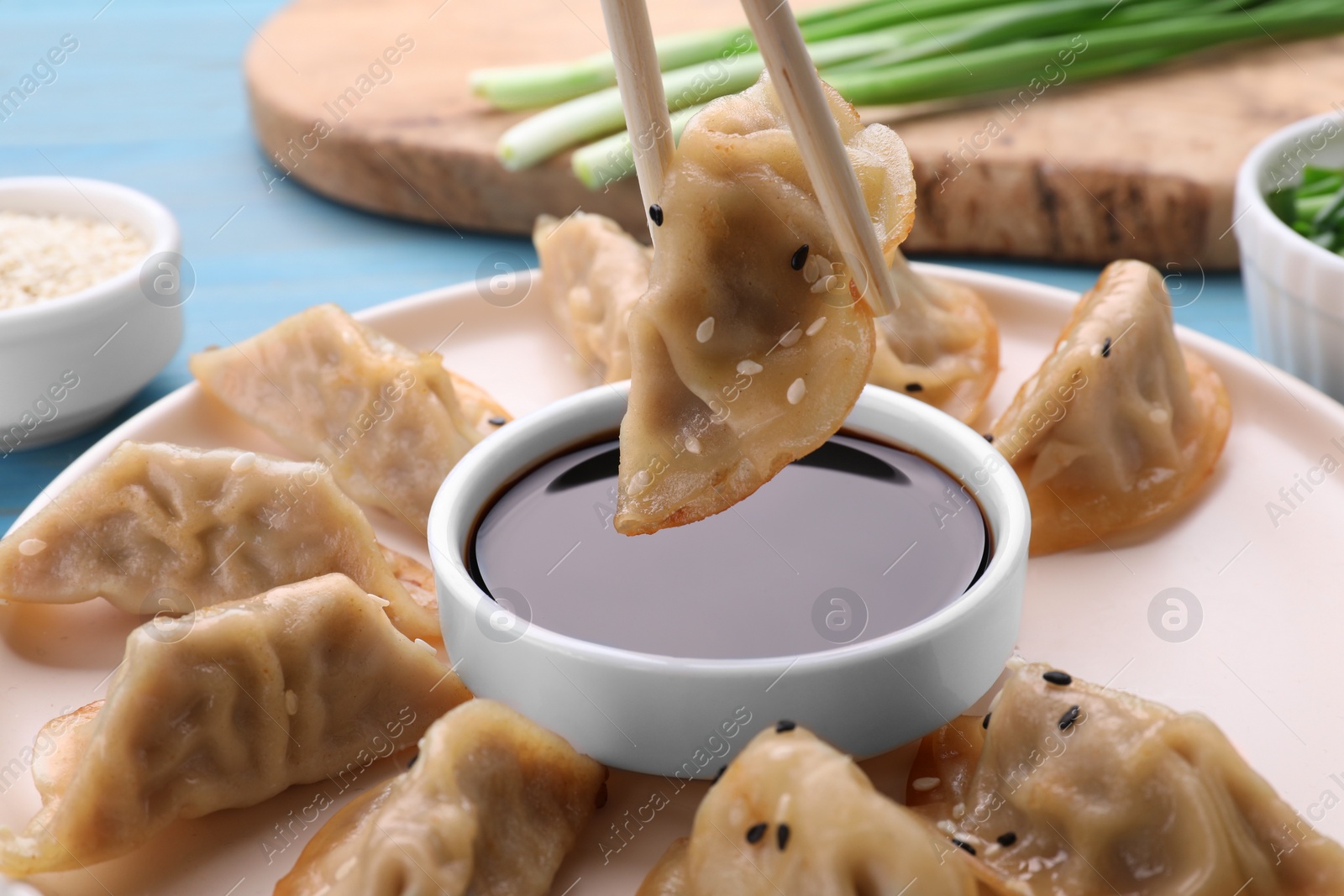 Photo of Holding delicious gyoza (asian dumpling) with chopsticks above soy sauce on table, closeup