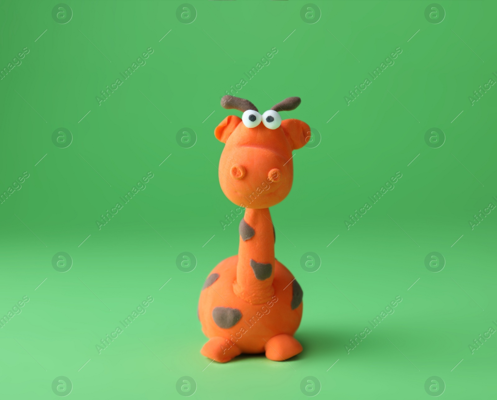 Photo of Small giraffe made from play dough on green background