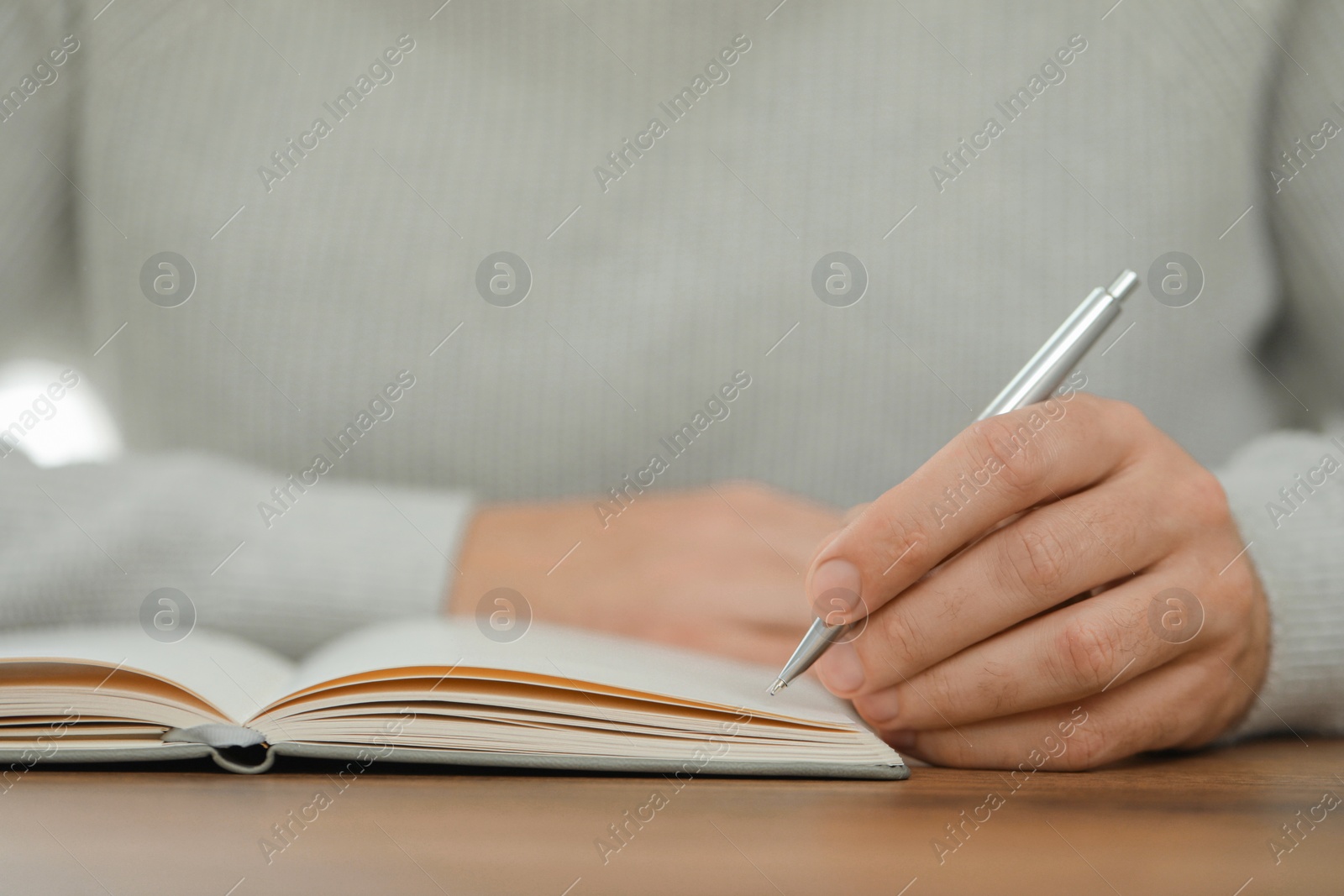 Photo of Man writing in notebook at wooden table, closeup