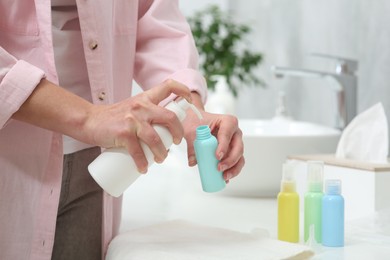 Photo of Woman pouring cosmetic product into plastic bottle over white countertop in bathroom, closeup and space for text. Bath accessories