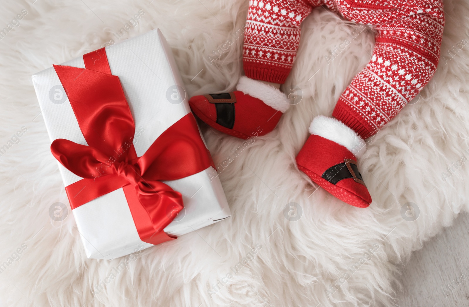 Photo of Cute baby in Christmas costume with gift box on fur rug