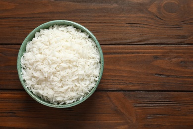 Bowl of tasty cooked rice on wooden background, top view. Space for text