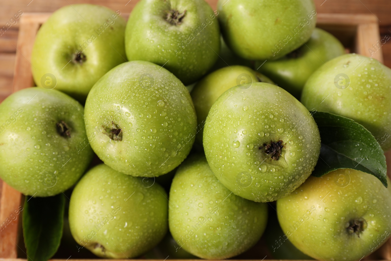 Photo of Fresh ripe green apples with water drops in crate, closeup