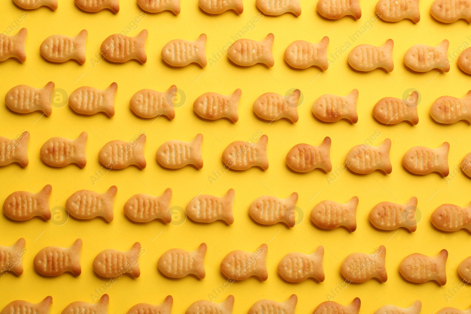Photo of Delicious goldfish crackers on yellow background, flat lay