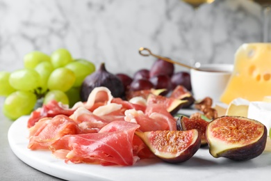 Delicious ripe figs and prosciutto served on grey table, closeup