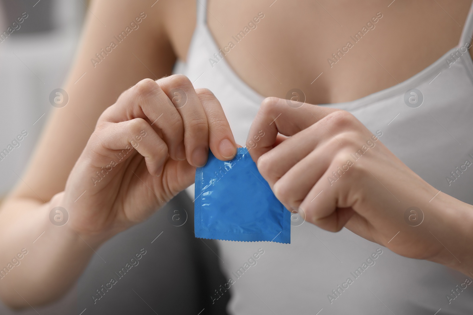 Photo of Woman opening condom indoors, closeup. Safe sex