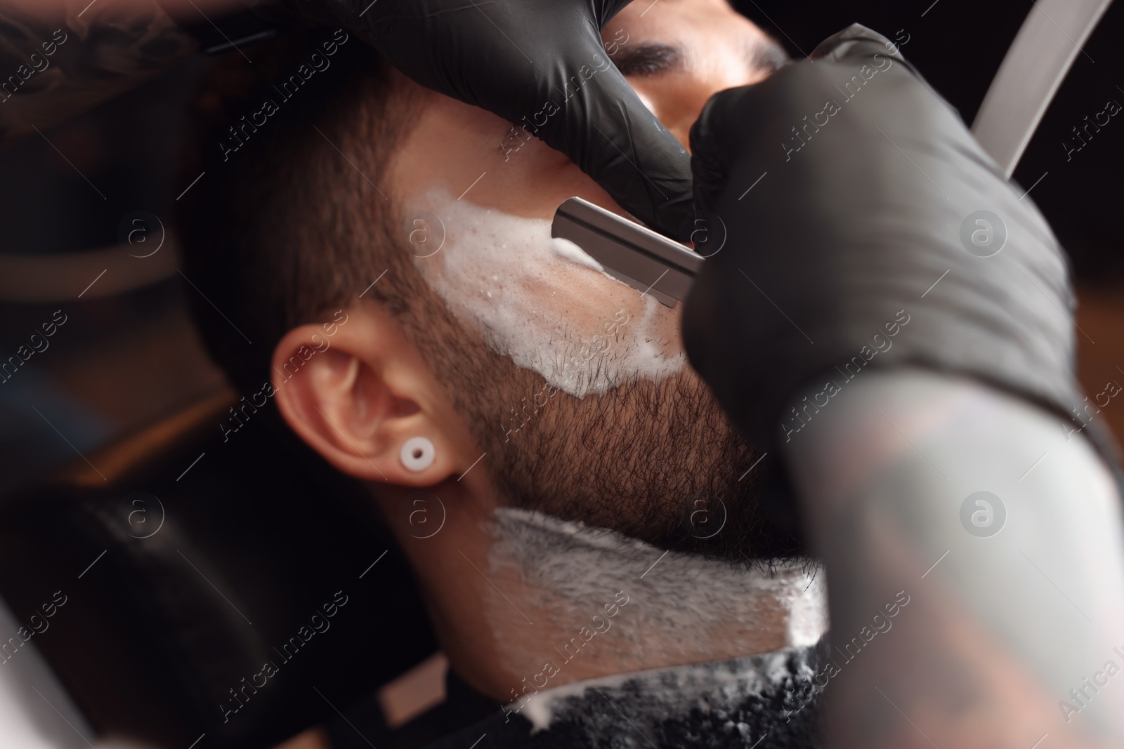 Photo of Professional hairdresser working with bearded client in barbershop, closeup