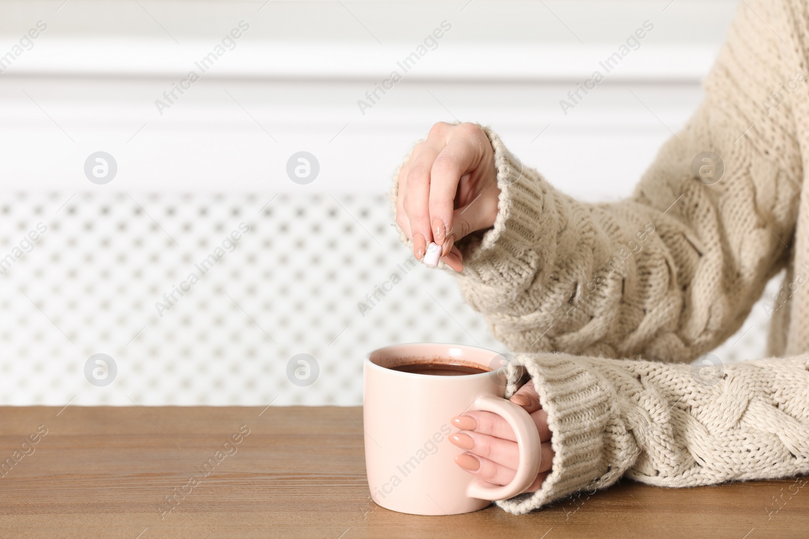 Photo of Woman in sweater holding cup of aromatic cacao on wooden table, closeup. Space for text