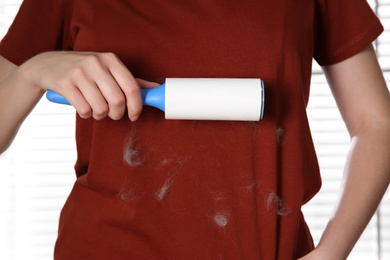 Photo of Woman removing cat hair from red t-shirt with lint roller near window, closeup