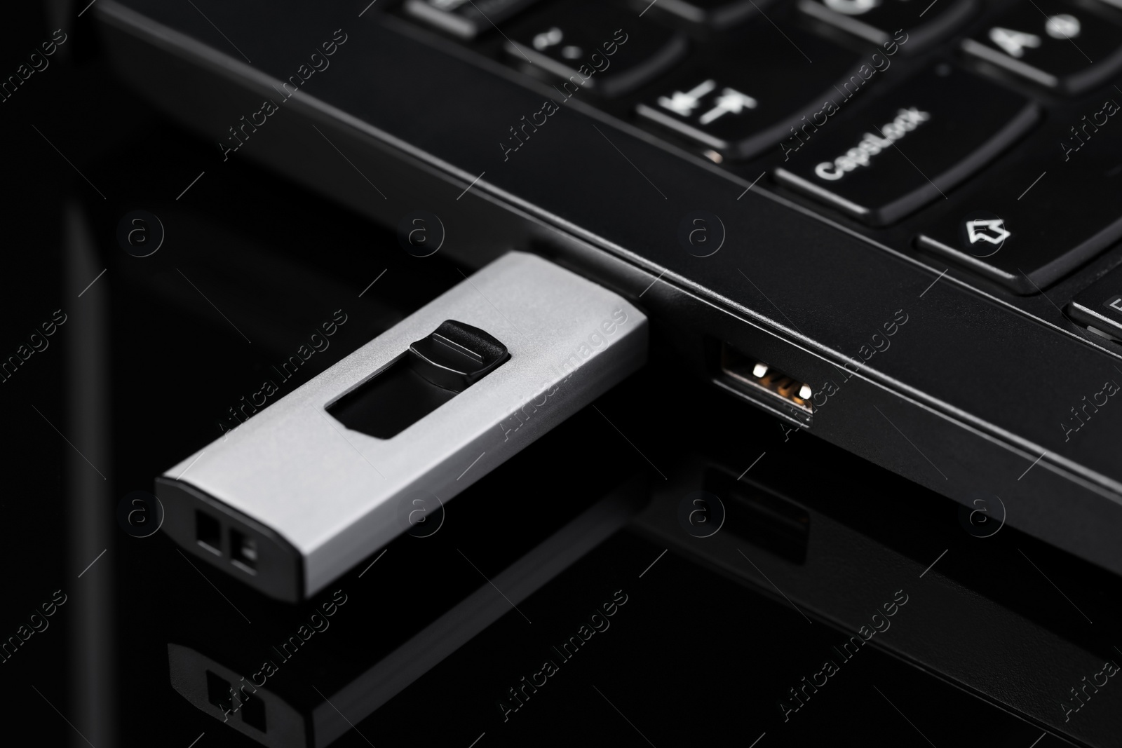 Photo of Modern usb flash drive attached into laptop on black table, closeup