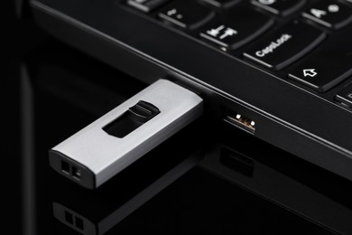 Modern usb flash drive attached into laptop on black table, closeup