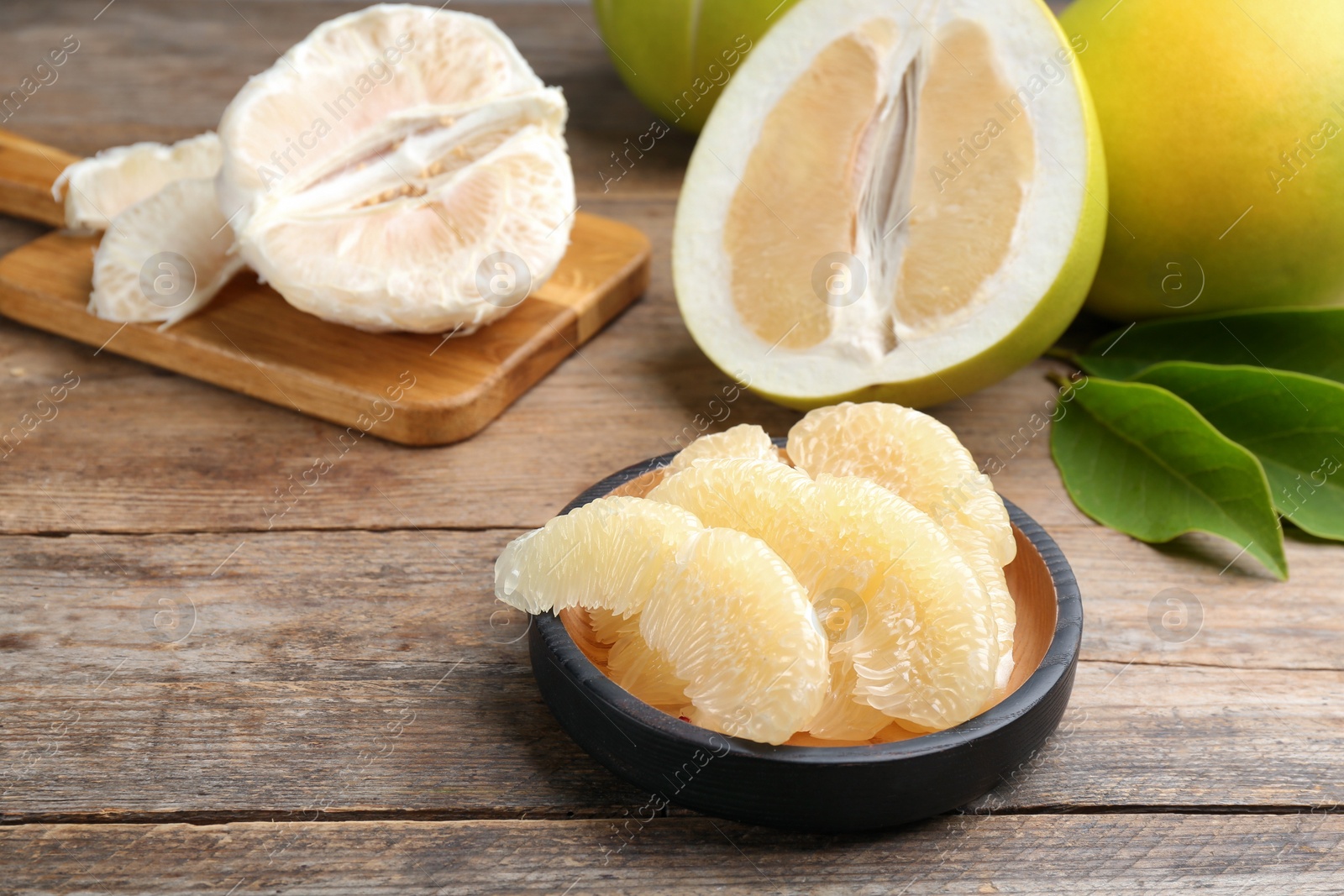 Photo of Bowl with peeled pomelo slices on wooden table, closeup